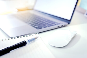 Working desk with a laptop, a mouse, a pen and a notebook.