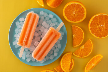 Orange popsicles on blue plate on yellow background	