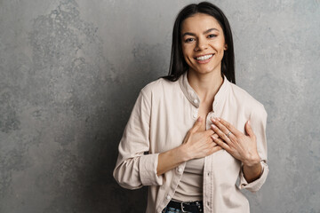 Brunette hispanic woman holding hands on her chest and smiling