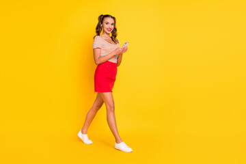 Fototapeta na wymiar Photo of charming girl walk hold phone wear striped shirt mini skirt sneakers isolated yellow color background