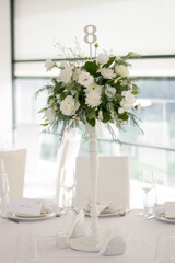 Centerpiece made of green leaves and fresh flowers stands on the dinner table. Wedding day. Fresh flowers decorations.