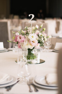 Centerpiece made of pink and white flowers stands in the middle of festive dinner table.