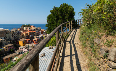 Fototapeta na wymiar Manarola, Liguria, Italy. June 2020. Panoramic view of the seaside village. The panoramic path runs parallel to the building: the colorful houses are picturesque. Beautiful summer day.