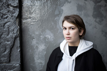 Fototapeta premium A serious short-haired girl in a white hoodie with a hood, a black raincoat and jeans walks down the street.