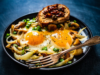 Continental breakfast - sunny side up eggs on white mushrooms, onion and  tomato bruschetta on black table
