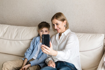 Boy and adult woman take a selfie on the phone while sitting on the couch.