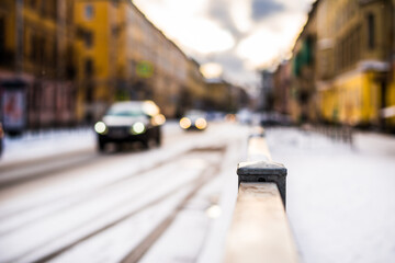 Bright winter sun in a big city, the headlights of the approaching cars in the snowfall. Close up view from the handrail on the sidewalk level