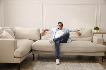 Fototapeta na wymiar Man with headphones sitting on comfortable sofa in living room
