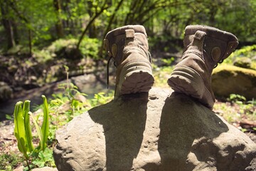 Fototapeta na wymiar An experienced tourist's boots are drying in the sun on a warm spring day on a stone in the forest. Shallow depth of field. A large black beetle climbs the stone. Travel atmosphere.