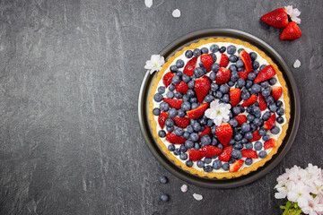 Fototapeta na wymiar Delicious blueberry and strawberry tart with whipped cream and mascarpone on a dark stone background. Top view. Copy space.