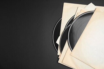 Vintage vinyl records in paper sleeves on black background, flat lay. Space for text