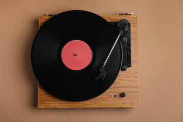 Modern vinyl record player with disc on brown background, top view