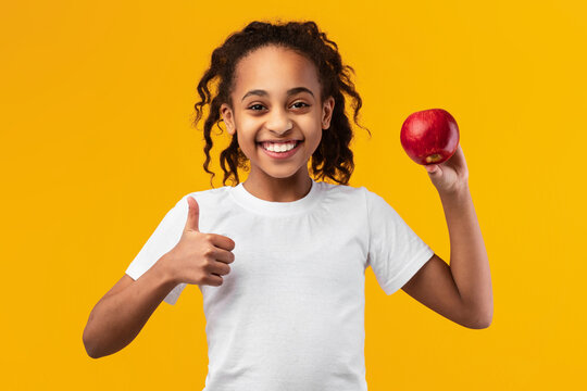 Portrait of a cheerful black girl holding red apple