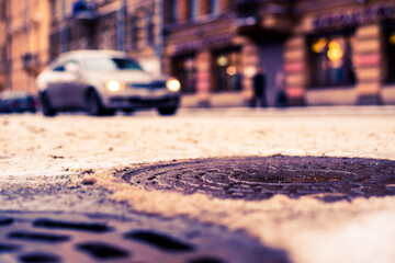 Snowy winter in the big city, the cars traveling on a busy street. Close up view of a hatches at the level of the asphalt