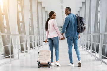 Fototapeta na wymiar Couple Travelling Concept. Romantic Black Spouses Walking With Luggage In Airport