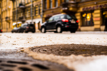 Snowy winter in the big city, the cars traveling on a busy street. Close up view of a hatches at the level of the asphalt