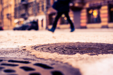 Fototapeta premium Snowy winter in the big city, a pedestrian crossing the road. Close up view of a hatches at the level of the asphalt