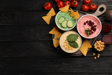 Fototapeta na wymiar Different kinds of tasty hummus served with nachos and ingredients on black wooden table, flat lay. Space for text