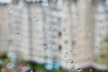 Raindrops on the glass close-up. Behind them is a blurry background of houses.