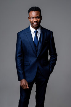 Smiling young handsome African man wearing formal business suit standing with hand in pocket on studio gray isolated background