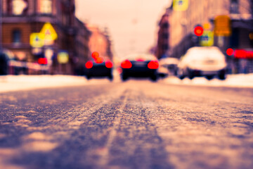 Snowy winter in the big city, the cars stopped at red traffic light signal. Close up view from the asphalt level