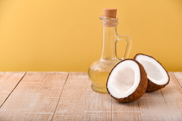 a bottle of coconut oil on a white wooden table with coconut halves on a yellow background with copy space