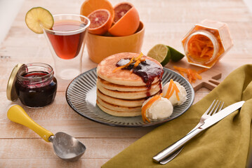 breakfast of pancakes with ice cream currant jam and tea with lime on a white wooden plate with a green linen napkin