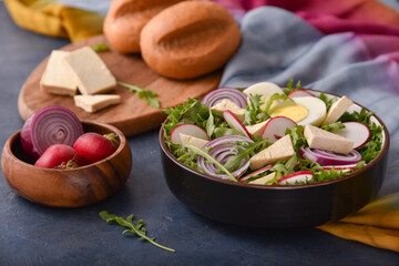 fresh vegetable and egg salad with cheese in brown bowl on blue stone table with colorful napkin and bread on wooden board