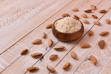 almond flour in a wooden bowl on a white wooden table with nuts