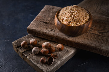 hazelnut flour in a wooden bowl on a wooden platform on a dark background