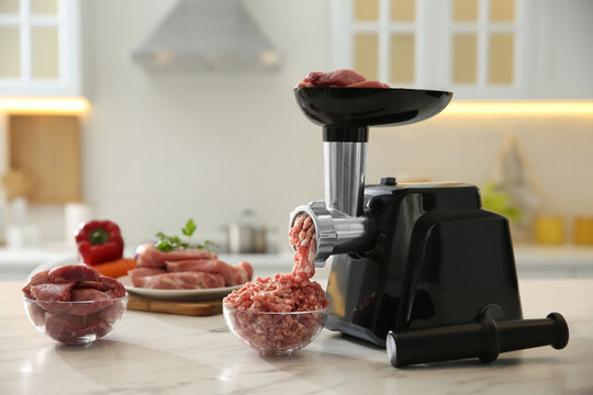 Modern meat grinder and products on white marble table in kitchen. Space for text