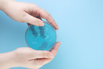 Liquid transparent gel for cleansing the face in a transparent jar in female hands, on a blue background. A moisturizing cosmetic product for skin or hair care.