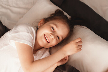 Obraz na płótnie Canvas Happy little girl on bed at home smiling and looking at camera. Leisure time concept