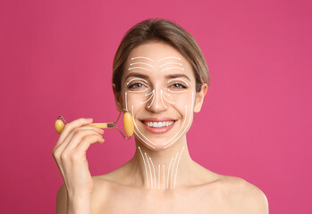 Woman using natural jade face roller on pink background