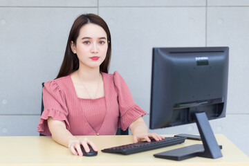 Asian business woman who wears pink dress working in an office typing on a keyboard and mouse.