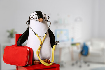 Toy penguin with eyeglasses, stethoscope and first aid bag indoors, space for text. Pediatrician...