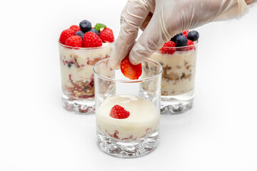 Muesli with yogurt and berries in a glass On a white background. The chef's hand puts strawberry slices into the dessert. Dessert decoration. Dessert preparation process.Fitness food. 