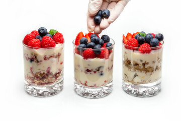 Muesli with yogurt and berries in a glass On a white background. The chef's hand puts blueberry into the dessert. Dessert preparation process. Fitness food. 