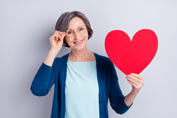 Photo portrait of cheerful granny showing love symbol red heart smiling in glasses isolated on grey color background