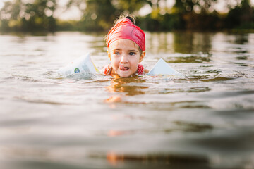 Happy summertime, healthy childhood, sport concept. Close up portrait of girl with red kerchief swimming in river in hot summer day. Soft focus. Horizontal shot.