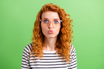 Photo of impressed sweet young woman wear striped shirt spectacles sending you kiss isolated green color background