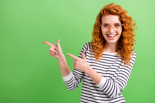 Photo of adorable cute lady dressed striped clothes glasses smiling pointing two fingers empty space isolated green color background