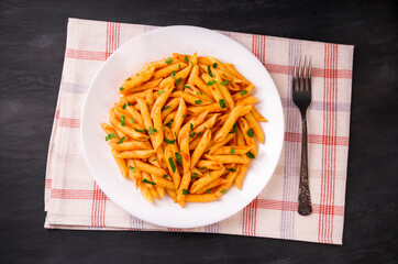 Penne pasta in tomato sauce, decorated with parsley on a black background