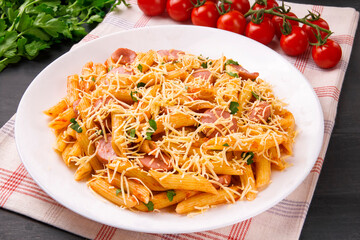 Penne pasta in tomato sauce with sausages and cheese, decorated with parsley on a  black background