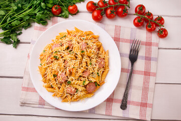 Penne pasta in tomato sauce with sausages and cheese, decorated with parsley on a white wooden table
