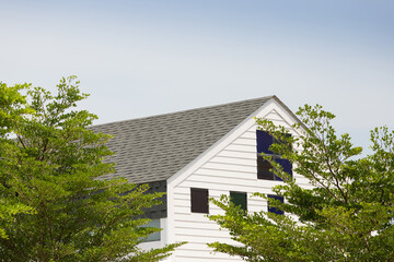 Roof shingles on top of the wooden house among a lot of trees. dark asphalt tiles on the roof background.