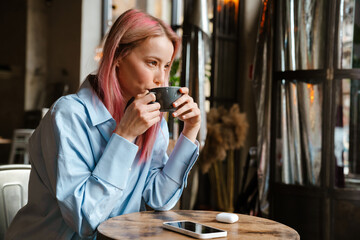 Young white woman with pink hair drinking coffee while sitting in cafe