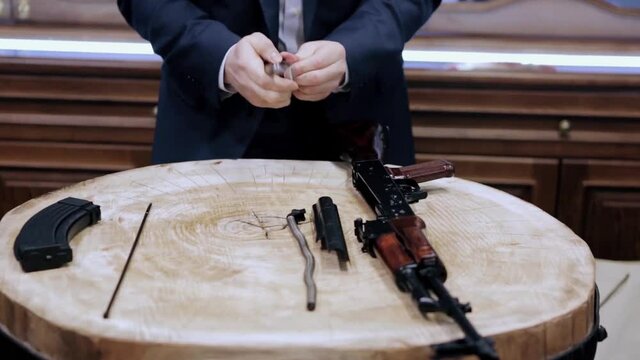 Process of assembly of the Kalashnikov rifle. Video. Close up of man dressed in official suit assembling the automatic gun during special event.