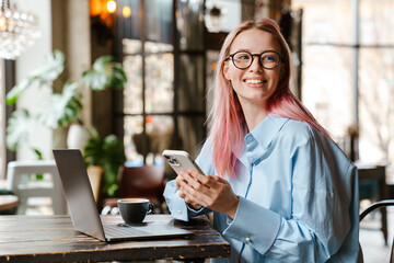 Fototapeta premium Young woman using laptop and cellphone while sitting in cafe