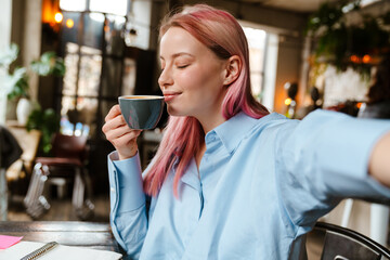 Young woman taking selfie photo while drinking coffee in cafe